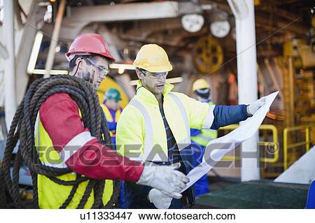 Stock Photo - Workers examining blueprints on oil rig. Fotosearch
