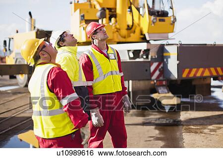 Stock Photograph - Workers on oil rig examining crane. Fotosearch