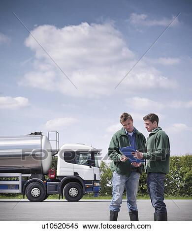Stock Photography - Workers reading clipboard by tanker. Fotosearch