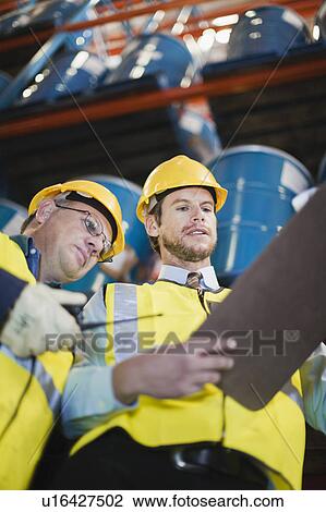 Stock Image - Workers reading clipboard in warehouse. Fotosearch
