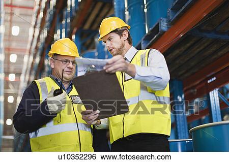 Workers reading clipboard in warehouse View Large Photo Image Stock Photograph - Workers reading clipboard in warehouse. Fotosearch
