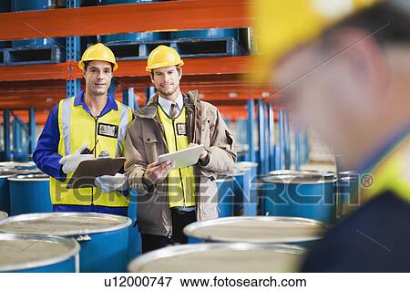 Stock Photo - Workers reading clipboards in warehouse. Fotosearch