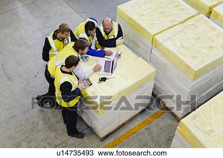 Stock Image - Workers using laptop in warehouse. Fotosearch