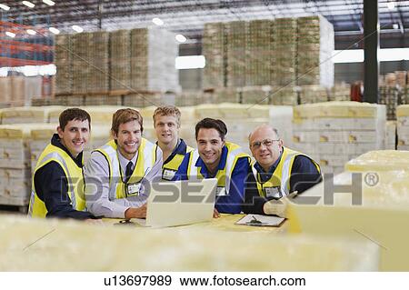 Stock Photo - Workers using laptop in warehouse. Fotosearch