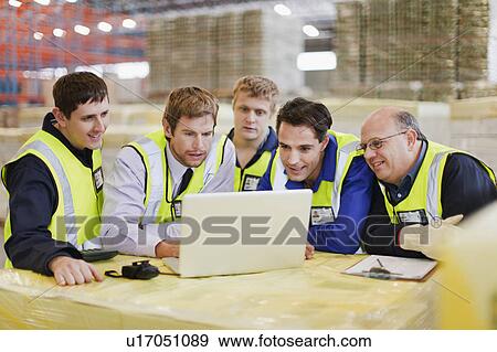 Stock Photo - Workers using laptop in warehouse. Fotosearch