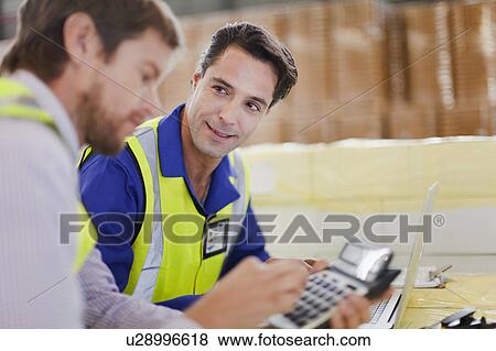 Stock Photo - Workers using laptop in warehouse. Fotosearch