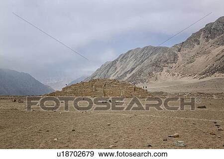 Stock Photo - Caral ancient ruins: temple mounds with mountains beyond, stormy sky, Supe Valley, Peru. Fotosearch