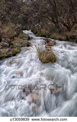 Stock Photo - Close up: mountain stream with motion blur, and snow-capped mountains beyond, blue sky, Cordilleras, Peru. Fotosearch