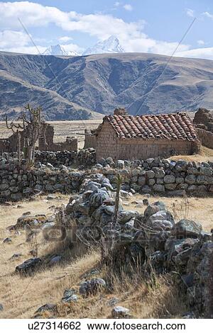 Stock Image - Cordilleras mountains: remains of rural stone hut, stone walls on grassy hillside, with snow-capped mountains beyond, Peru. Fotosearch