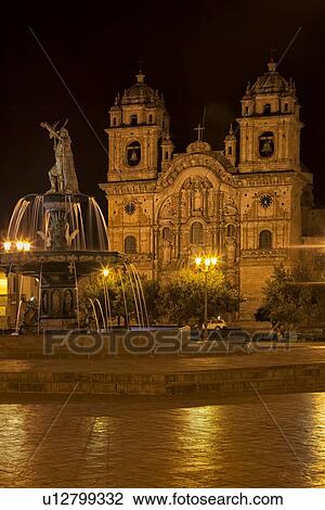 Stock Image - Cuzco by night: Plaza de Armas with Catedral seen beyond central fountain with bronze statue of Manco Inca, Cuzco, Peru. Fotosearch