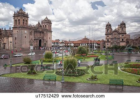 Stock Photo - Cuzco: Plaza de Armas, view of Catedral and Iglesia de la Compania, central fountain with statue, people walking after afternoon rain shower, blue sky with dramatic clouds, Cuzco, Sacred Valley, Peru. Fotosearch