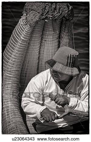 Stock Image - Lake Titicaca: islands of Uros with closeup monochrome portrait of man in traditional costume rowing reed boat, Peru. Fotosearch
