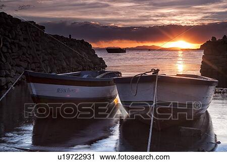 Stock Image - Lake Titicaca: Llachon peninsula, two fishing boats moored at sunset in harbour inlet, Peru. Fotosearch