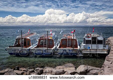 Stock Image - Lake Titicaca: Taquile island harbour with four boats moored, dramatic clouds and blue sky, Peru. Fotosearch