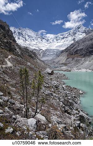 Stock Photograph - Llaca valley: glacier and moraine, with river and snow-capped mountains beyond, blue sky, Cordilleras, Peru. Fotosearch