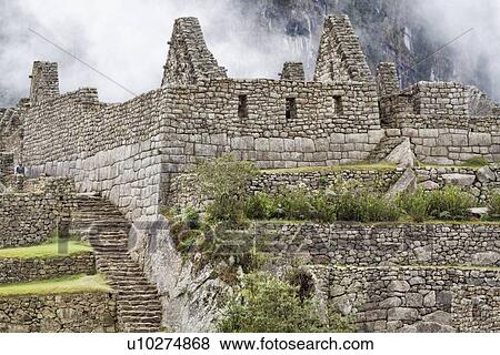 Stock Photo - Machu Picchu Inca ruins: detail of agricultural sector terraces and buildings with steep mountain wall beyond in mist, Machu Picchu, Sacred Valley, Peru. Fotosearch
