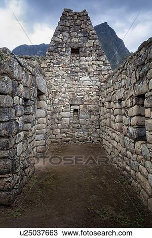 Stock Image - Machu Picchu Inca ruins: urban sector building with typical niches and trapezoidal windows, Machu Picchu mountain beyond, storm looming, Machu Picchu, Sacred Valley, Peru. Fotosearch
