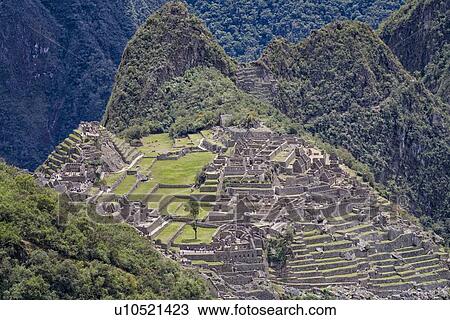 Stock Image - Machu Picchu Inca ruins: view of entire complex: Eastern Urban sector, Royal Palaces and Temple of the Sun, Intihuatana, with Huayna Picchu and ring of mountains beyond, as seen from Sun Gate, afternoon sunlight after storm, Machu Picchu, Sacred Valley, . Fotosearch