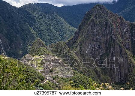 Stock Photo - Machu Picchu Inca ruins: view of entire complex: Eastern Urban sector, Royal Palaces and Temple of the Sun, Intihuatana, with Huayna Picchu and ring of mountains beyond, as seen from Sun Gate, afternoon sunlight after storm, Machu Picchu, Sacred Valley, . Fotosearch