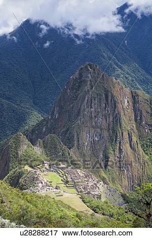 Stock Photo - Machu Picchu Inca ruins: view of entire complex: Eastern Urban sector, Royal Palaces and Temple of the Sun, Intihuatana, with Huayna Picchu and ring of mountains beyond, all seen from above on Machu Picchu mountain, afternoon sunlight after storm, Machu . Fotosearch