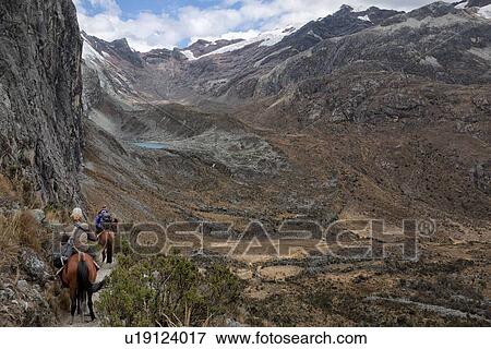 Stock Photo - Mountain trail with riders on horseback, near Laguna 69 showing surrounding glaciers of Pisco East and Pisco West, and unnamed turquoise lake, valley below, Cordilleras, Peru. Fotosearch