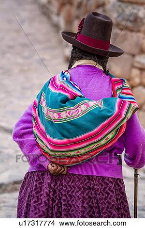 Picture - Older Peruvian lady seen close up from behind, walking in golden evening light, carrying colourful cloth bag and walking stick, Sacred Valley, Peru. Fotosearch