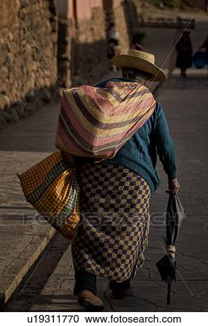 Older Peruvian lady seen close up from behind, walking in golden evening light, carrying colourful cloth bags and umbrella as walking stick, Sacred Valley, Peru View Large Photo Image Stock Image - Older Peruvian lady seen close up from behind, walking in golden evening light, carrying colourful cloth bags and umbrella as walking stick, Sacred Valley, Peru. Fotosearch