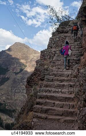 Stock Image - Pisac ruins: view of three hikers on steps of trail leading to Inca citadel with mountains of Sacred Valley beyond, sunny afternoon, blue skies, Sacred Valley, Cuzco, Peru. Fotosearch