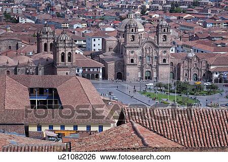 Stock Photograph - Plaza de Armas with Iglesia de la Compania facing, and Catedral to left, as seen across red tiled rooftops from San Cristobal, Cuzco, Peru. Fotosearch