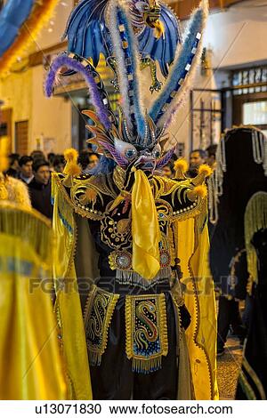 Stock Image - Puno: traditional street festa with formation dancing in ceremonial costume, detail of beautiful yellow costume and Inca mask, evening, Peru. Fotosearch
