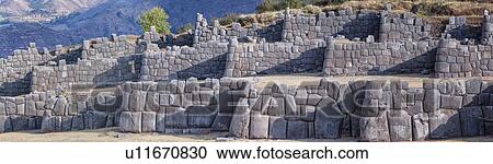 Stock Image - Sacsaywaman Inca ruins: panorama view of the massive zig zag stone wall fortifications in late afternoon sunlight, with strong triangular shadows, City of Cuszco beyond, Sacred Valley, Cuzco, Peru. Fotosearch