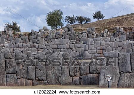 Sacsaywaman Inca ruins: view of the massive zig zag stone wall fortifications in late afternoon sunlight with tourist in foreground, Sacred Valley, Cuzco, Peru View Large Photo Image Picture - Sacsaywaman Inca ruins: view of the massive zig zag stone wall fortifications in late afternoon sunlight with tourist in foreground, Sacred Valley, Cuzco, Peru. Fotosearch