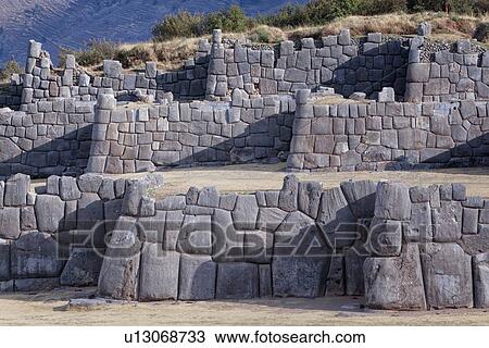 Stock Image - Sacsaywaman Inca ruins: view of the massive zig zag stone wall fortifications in late afternoon sunlight, with strong triangular shadows, Sacred Valley, Cuzco, Peru. Fotosearch