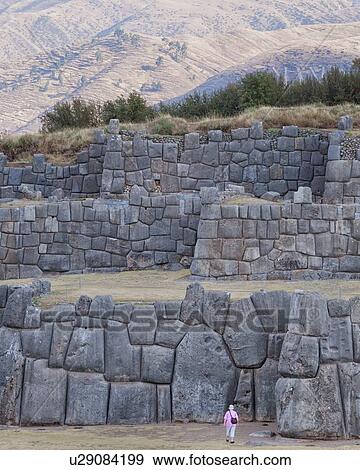 Stock Photo - Sacsaywaman Inca ruins: view of the massive zig zag stone wall fortifications in late afternoon sunlight with tourist in foreground, Sacred Valley, Cuzco, Peru. Fotosearch
