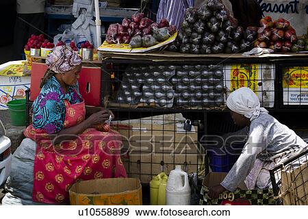 Stock Photo - Two women sitting sorting fruit at outdoor market in bright, colourful clothing, against backdrop of fruit stall, Nakuru, Kenya,. Fotosearch