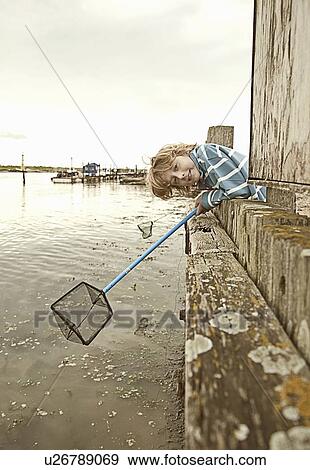 Stock Photo - Boy fishing with net on pier. Fotosearch
