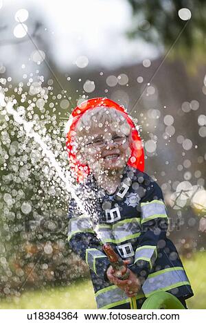 Picture - Boy in fireman costume playing with hose. Fotosearch