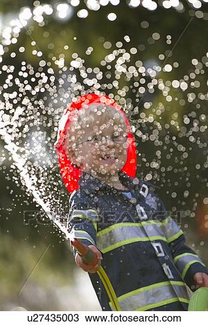 Stock Image - Boy in fireman costume playing with hose. Fotosearch