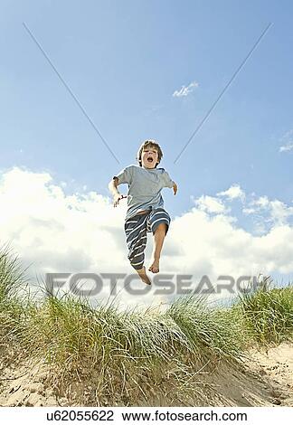 Stock Image - Boy leaping over grass on beach. Fotosearch