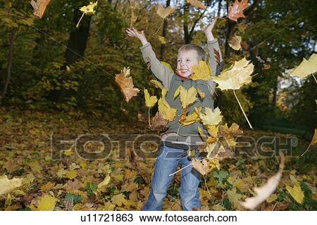 Stock Image - Boy playing in autumn leaves. Fotosearch