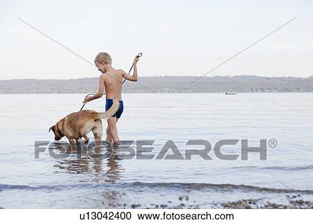 Boy wading with dog on beach View Large Photo Image Stock Image - Boy wading with dog on beach. Fotosearch