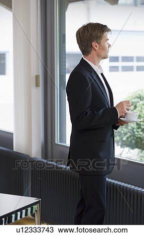 Businessman standing at window in office View Large Photo Image Stock Image - Businessman standing at window in office. Fotosearch
