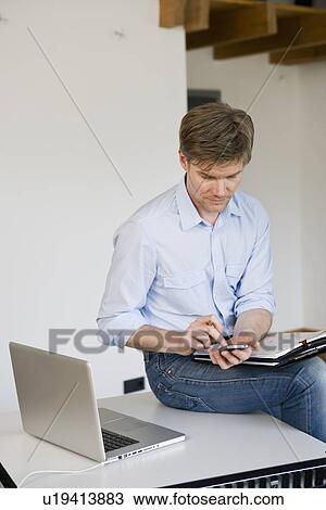 Stock Image - Businessman using cell phone in office. Fotosearch