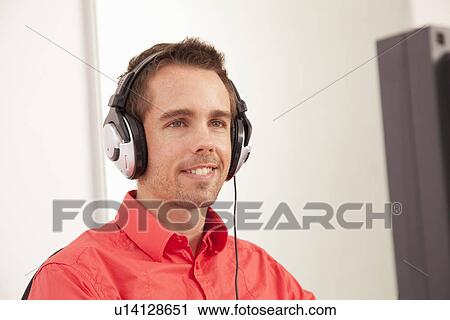 Stock Image - Businessman wearing headphones at desk. Fotosearch