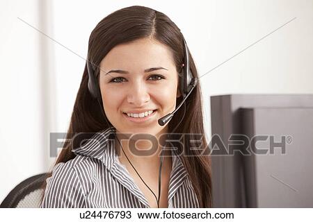 Stock Image - Businesswoman talking on headset at desk. Fotosearch