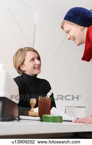 Businesswomen talking at desk in office View Large Photo Image Stock Image - Businesswomen talking at desk in office. Fotosearch