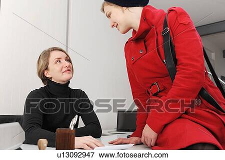 Stock Photo - Businesswomen talking at desk in office. Fotosearch