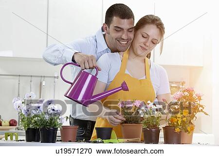 Stock Image - Couple watering potted plants indoors. Fotosearch