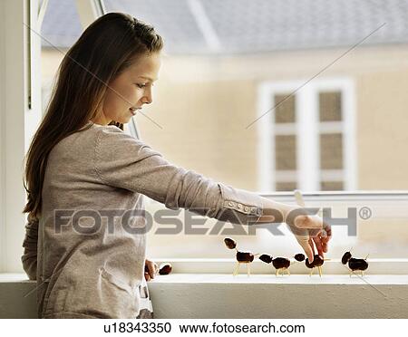 Stock Image - Girl arranging figurines on windowsill. Fotosearch