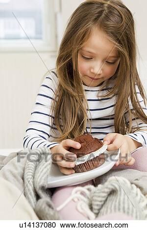 Stock Image - Girl eating chocolate muffin in bed. Fotosearch